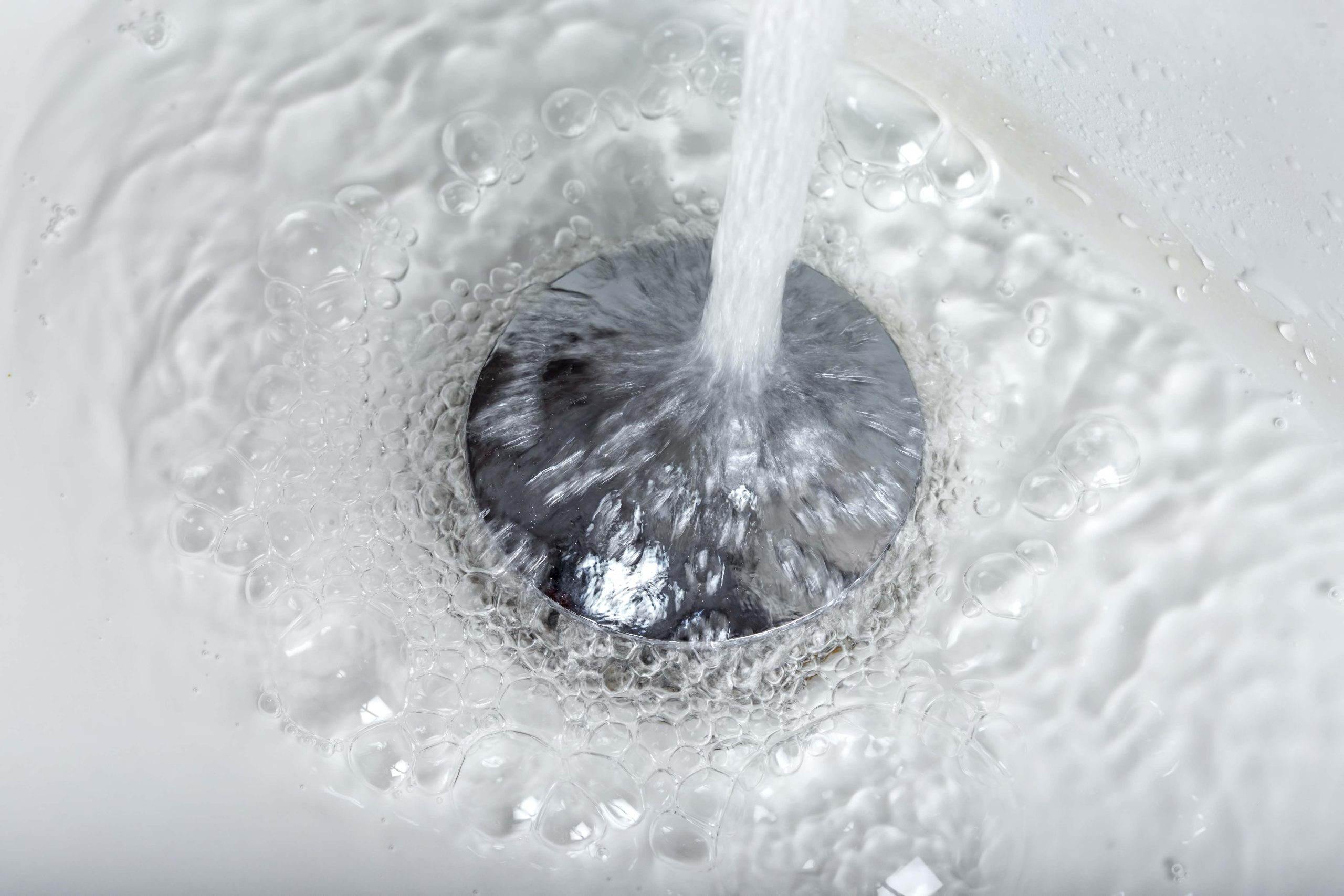 closeup of tap water flowing into stainless steel drain