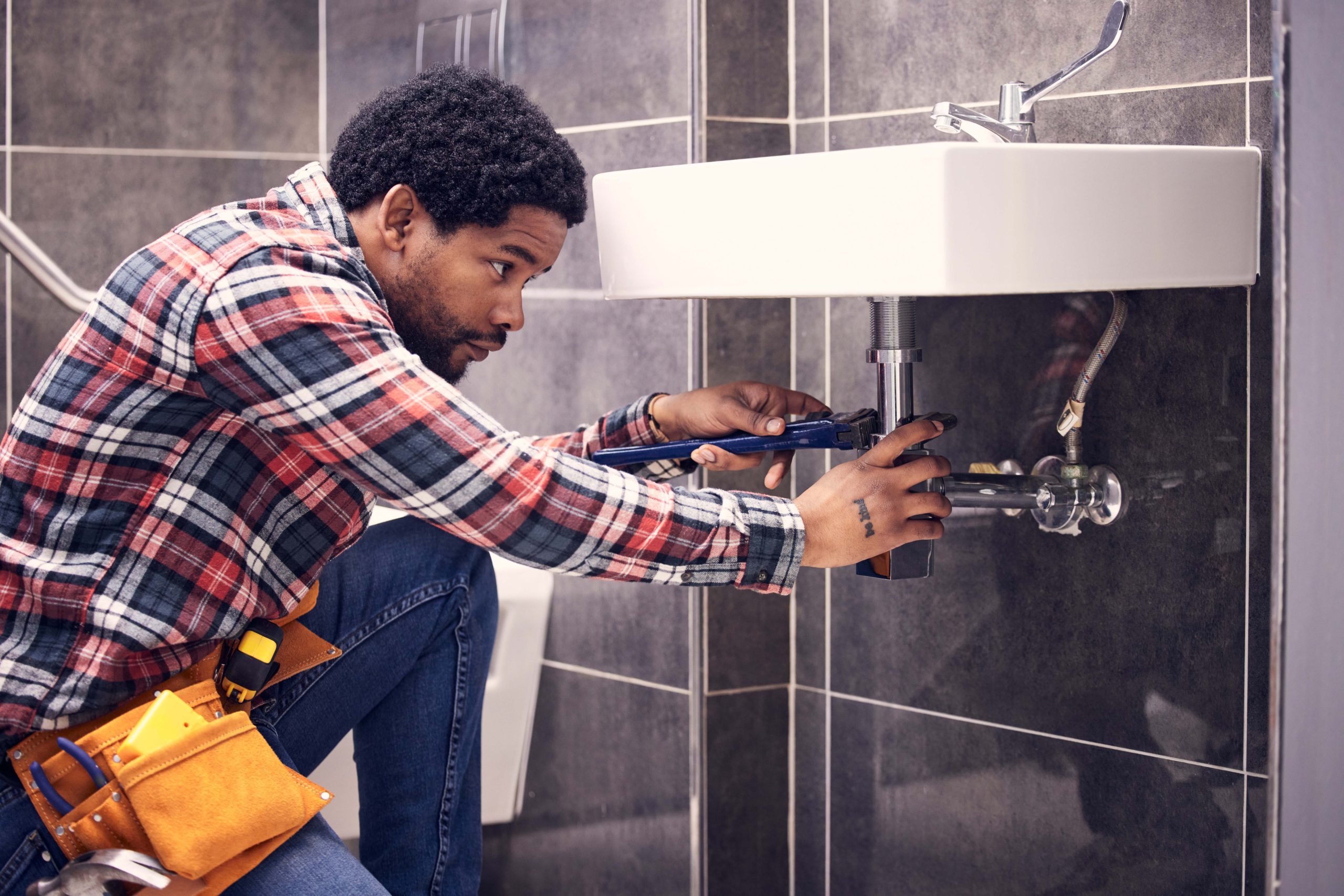 black man, plumber and maintenance in bathroom, fixing sink pipe